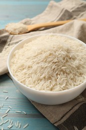 Photo of Raw basmati rice in bowl on light blue wooden table