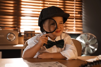 Cute little detective with magnifying glass at table in office