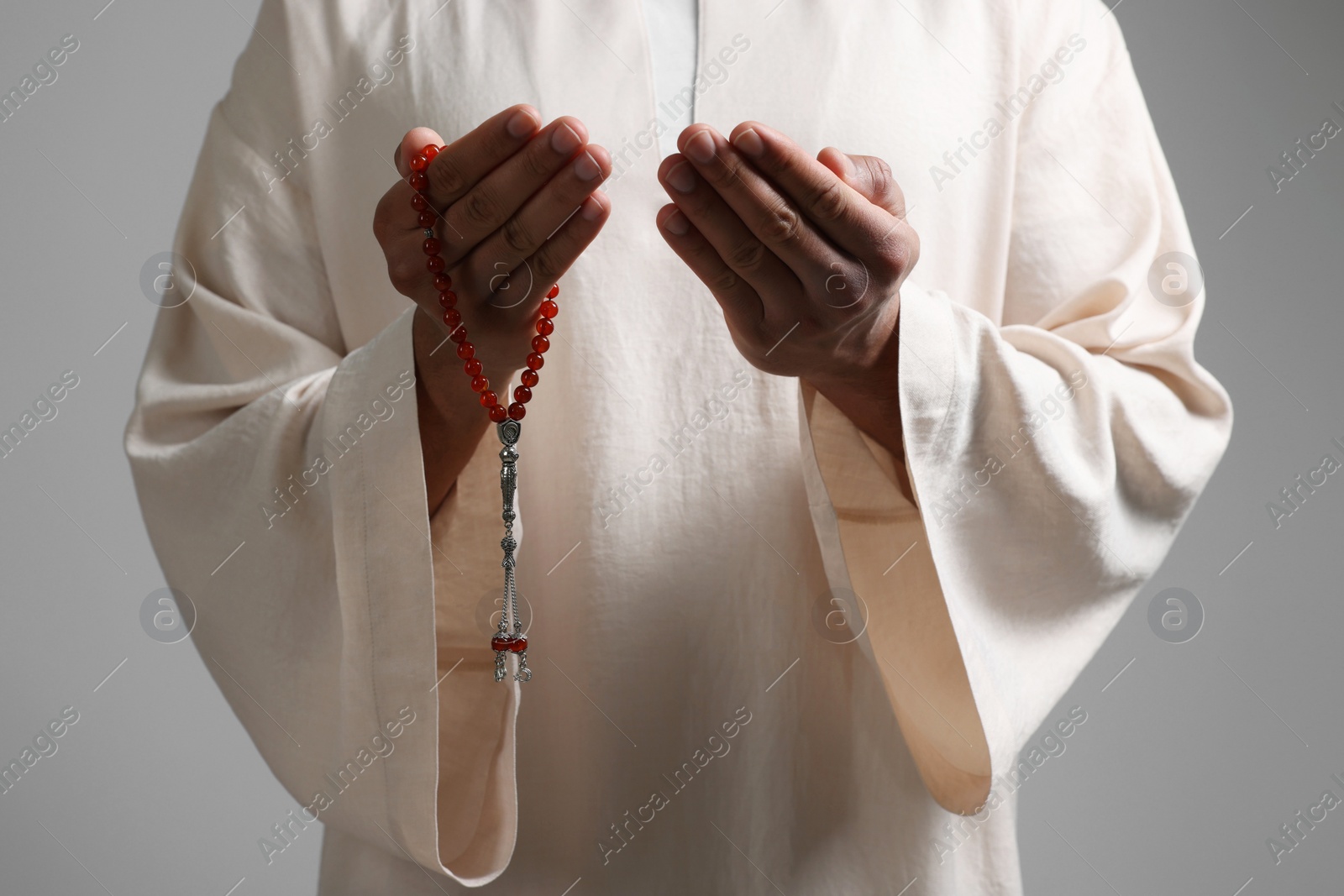 Photo of Muslim man with misbaha praying on light grey background, closeup