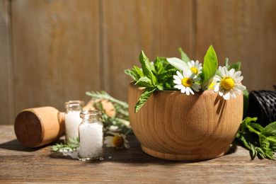 Photo of Mortar with chamomile flowers and fresh green mint on wooden table. Healing herbs