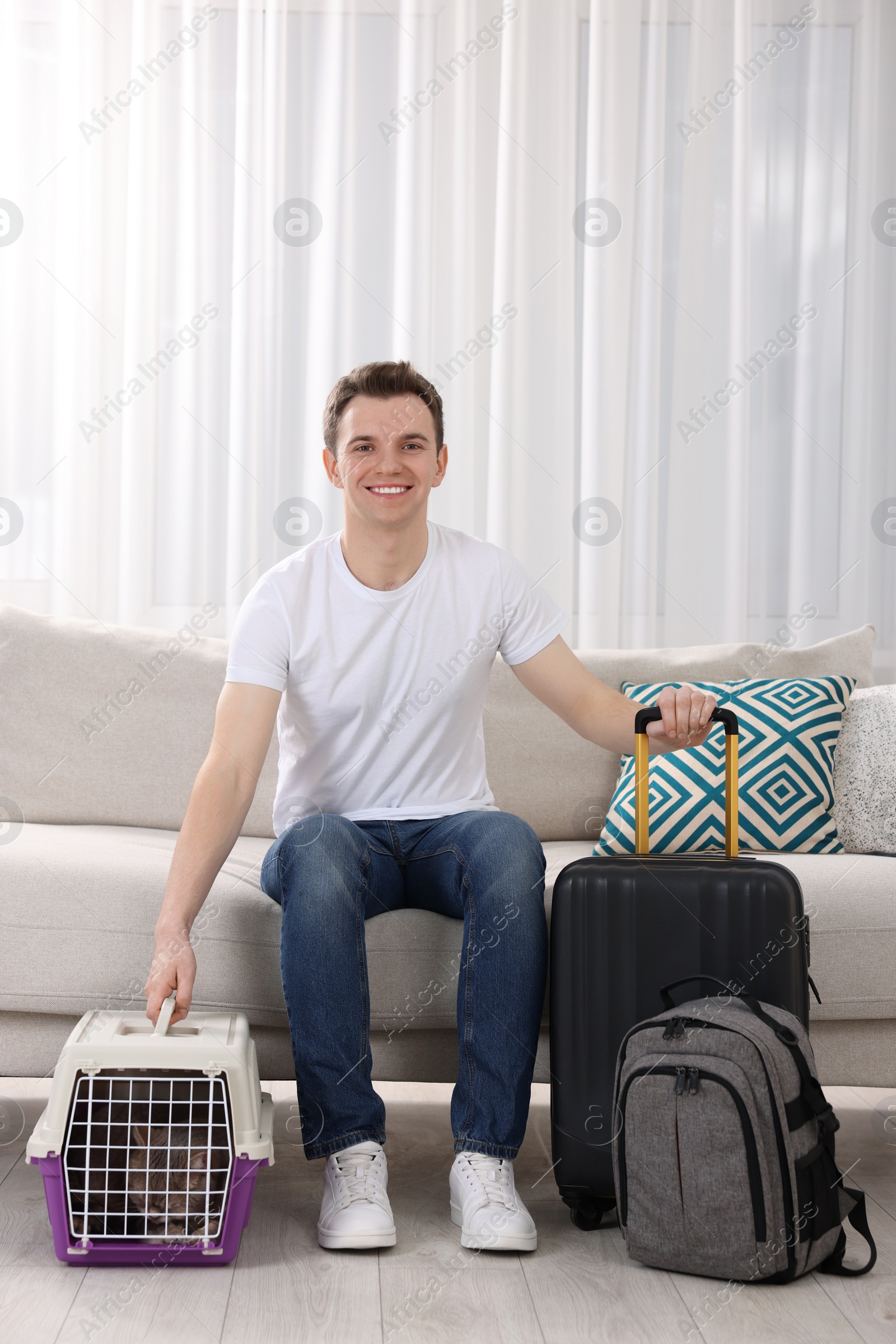 Photo of Travel with pet. Man near carrier with cute cat on sofa at home