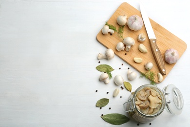 Photo of Glass jar of pickled mushrooms on white wooden table, flat lay. Space for text