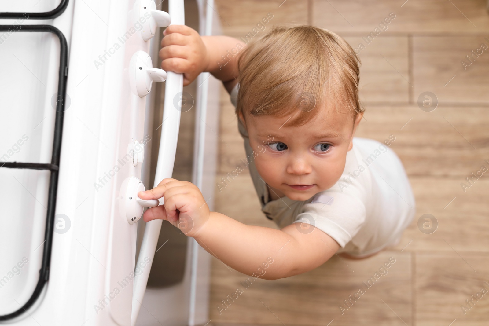 Photo of Little child playing with gas stove indoors, above view. Dangers in kitchen