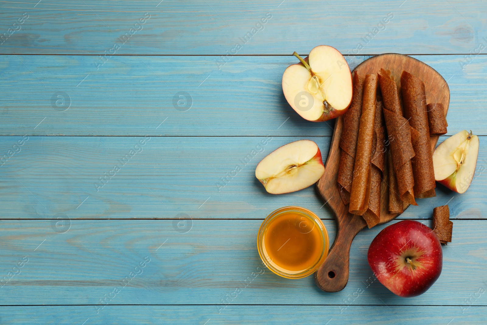 Photo of Flat lay composition with delicious fruit leather rolls on light blue wooden table. Space for text