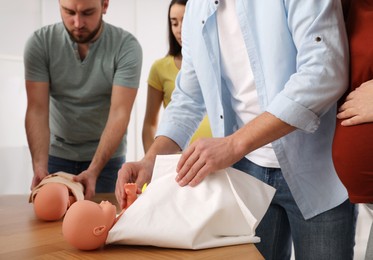 Photo of Future fathers and pregnant women learning how to swaddle baby at courses for expectant parents indoors, closeup