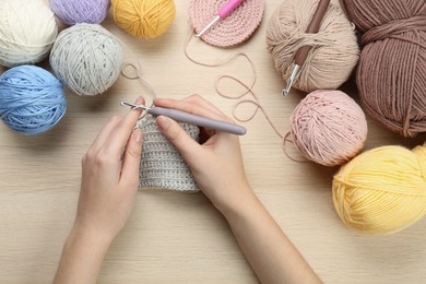 Woman crocheting with grey thread at wooden table, top view