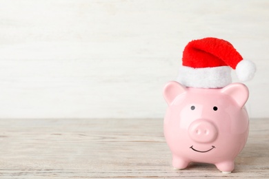 Photo of Piggy bank with Santa hat on table. Space for text