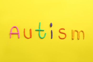 Photo of Word Autism made with colorful plasticine on yellow background, flat lay