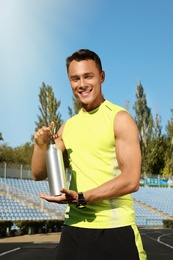 Sporty man with bottle of water at stadium on sunny day