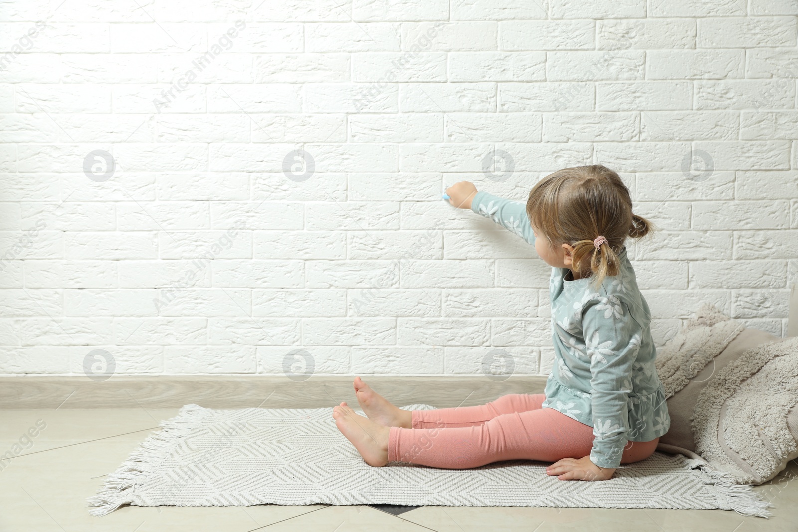 Photo of Little girl drawing on white brick wall indoors, space for text. Child`s art