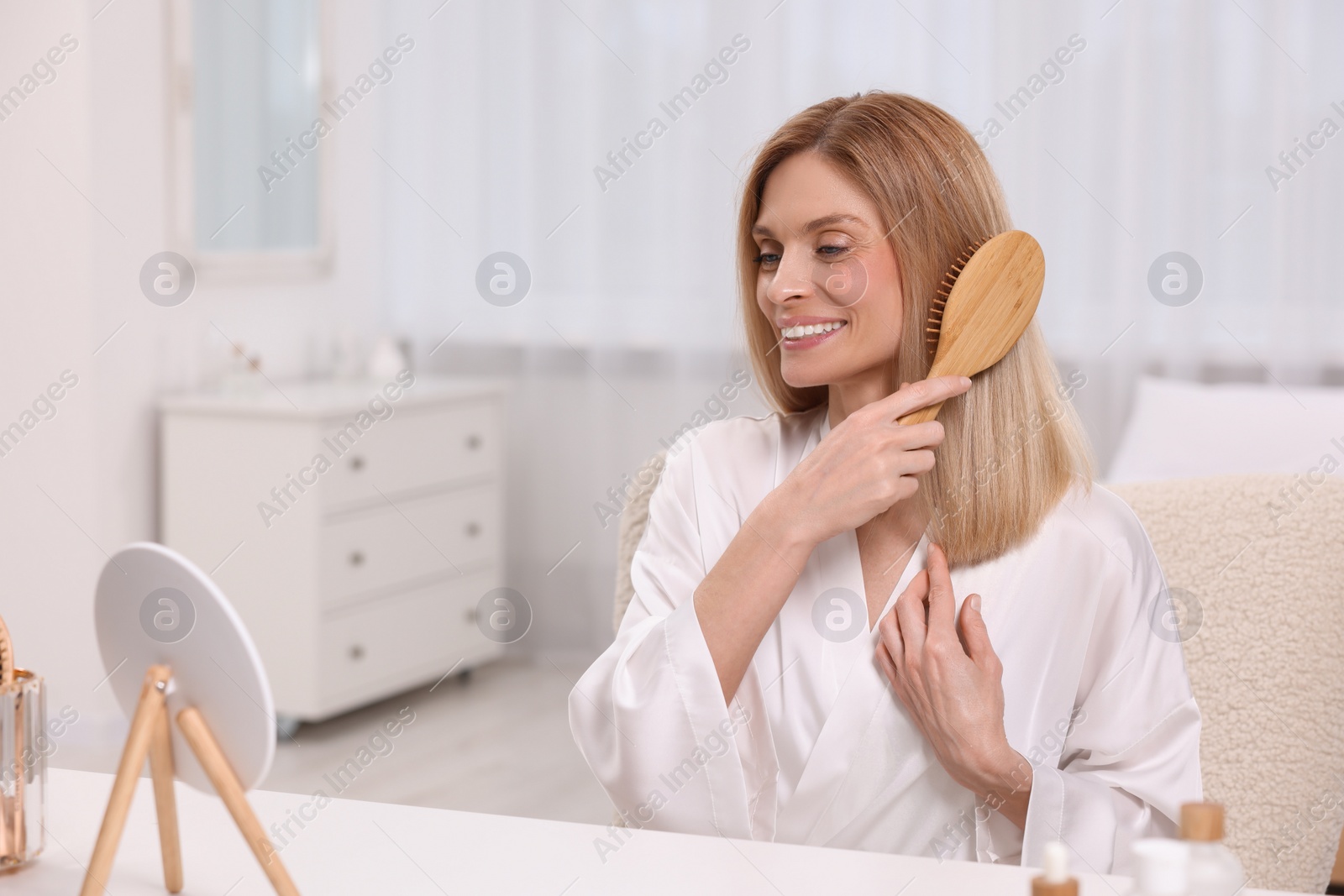 Photo of Beautiful woman brushing her hair at vanity in bedroom