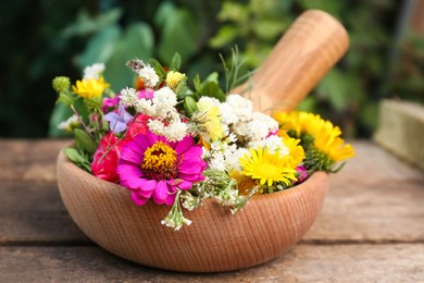 Mortar, pestle and different flowers on wooden table outdoors, closeup