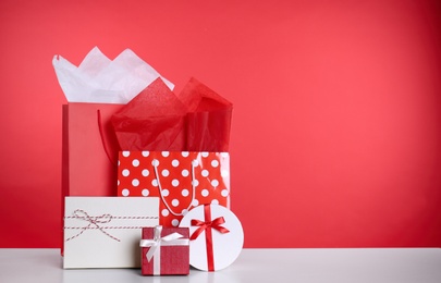 Photo of Shopping paper bags and gift boxes on red background. Space for text