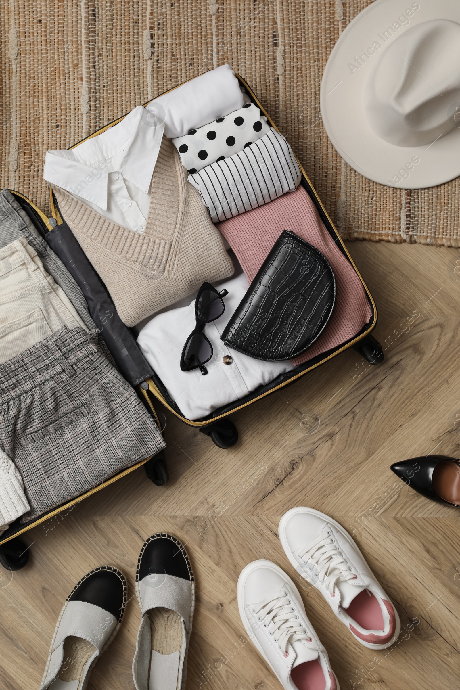 Photo of Open suitcase with folded clothes, accessories and shoes on floor, flat lay