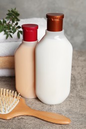 Photo of Bottles of shampoo, hairbrush and stacked towels on grey table, closeup