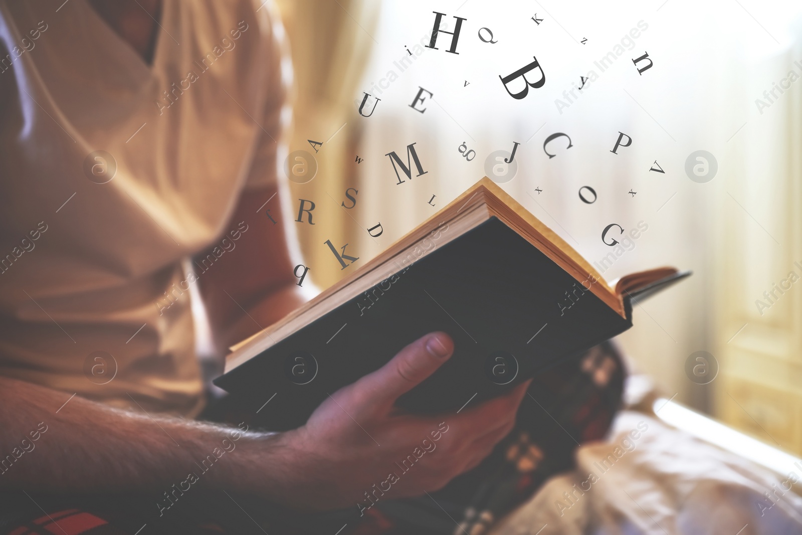 Image of Young man reading book with letters flying over it on bed at home, closeup