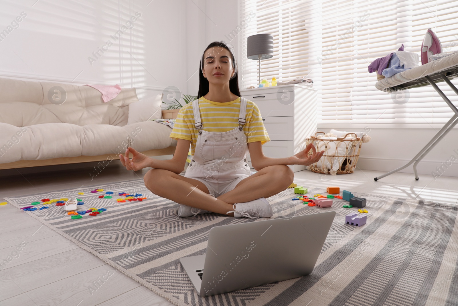 Photo of Calm young mother meditating on floor in messy living room