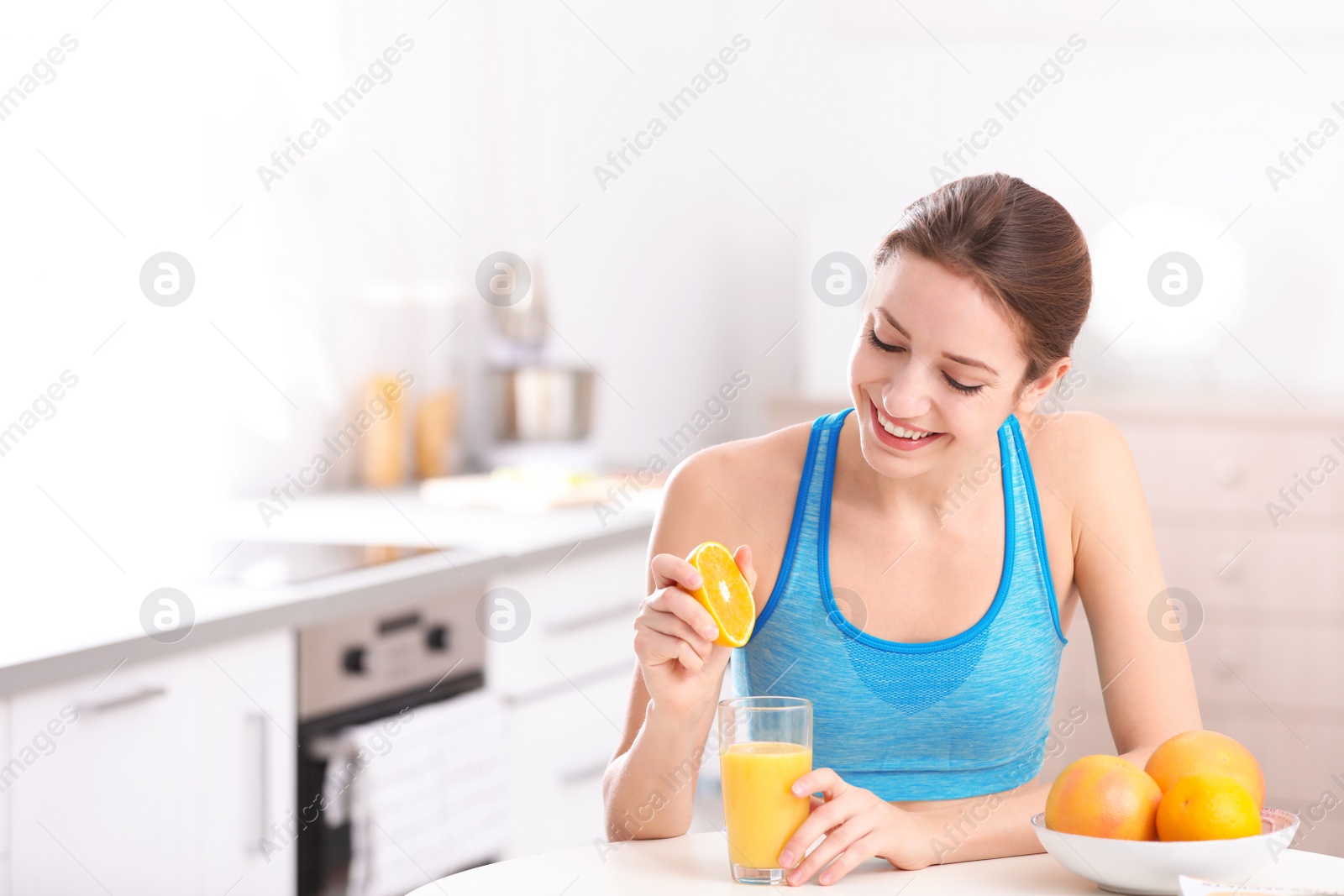 Photo of Young woman in fitness clothes making orange juice at home. Space for text