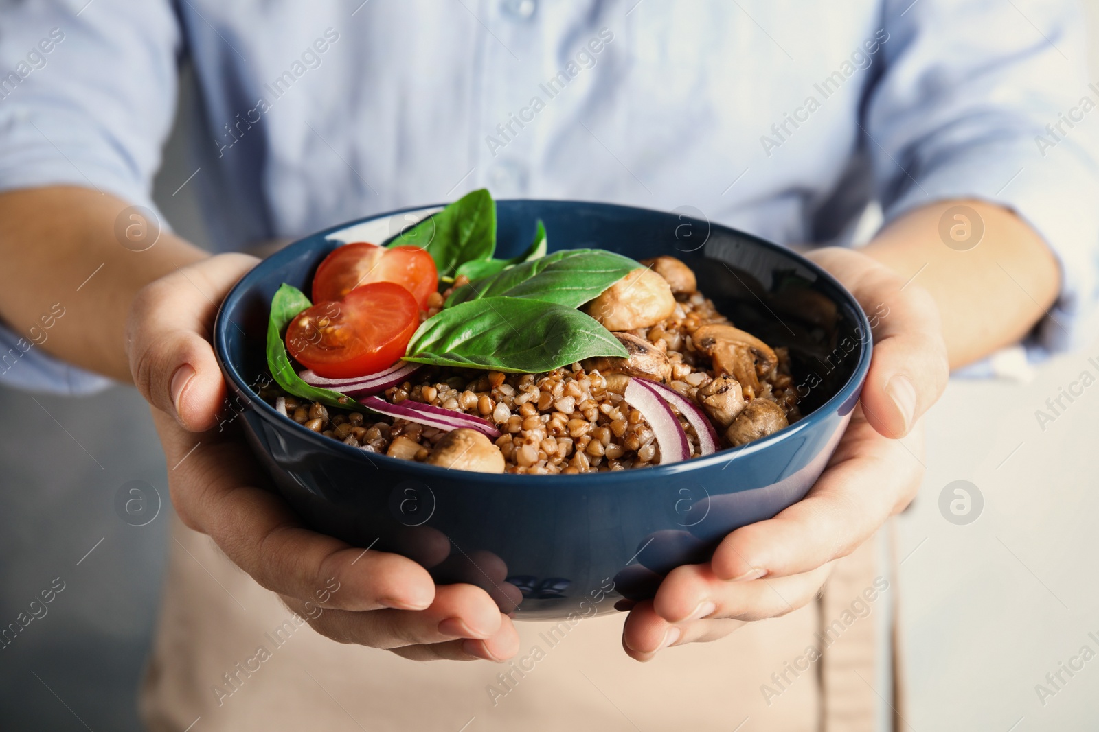 Photo of Woman holding bowl of delicious buckwheat porridge with vegetables and mushrooms, closeup