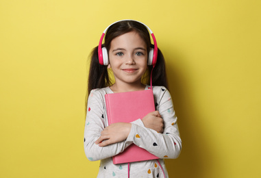 Photo of Cute little girl with headphones listening to audiobook on yellow background
