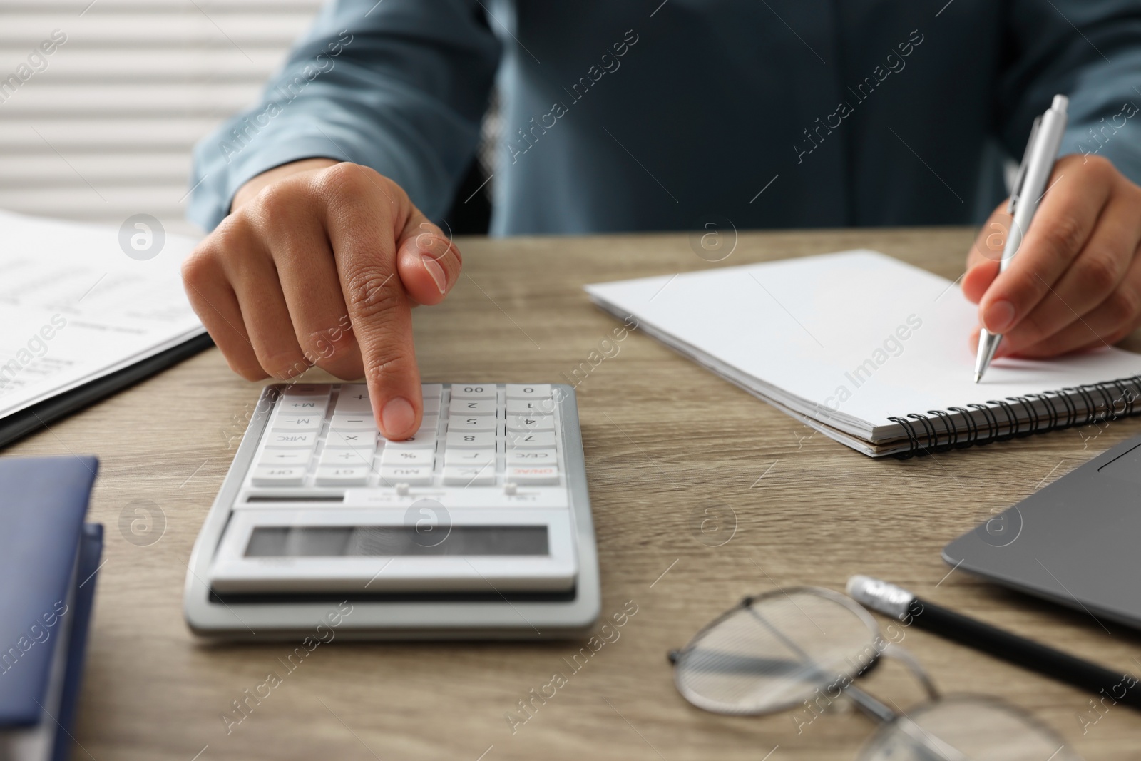 Photo of Woman using calculator while taking notes at wooden table, closeup