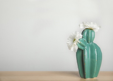 Trendy cactus shaped vase with flowers on table against light wall. Creative decor
