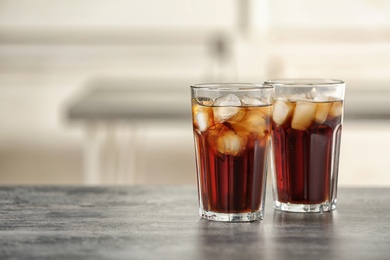 Glasses of cola with ice on table against blurred background, space for text