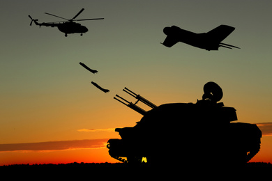 Image of Silhouettes of different military machinery at sunset outdoors