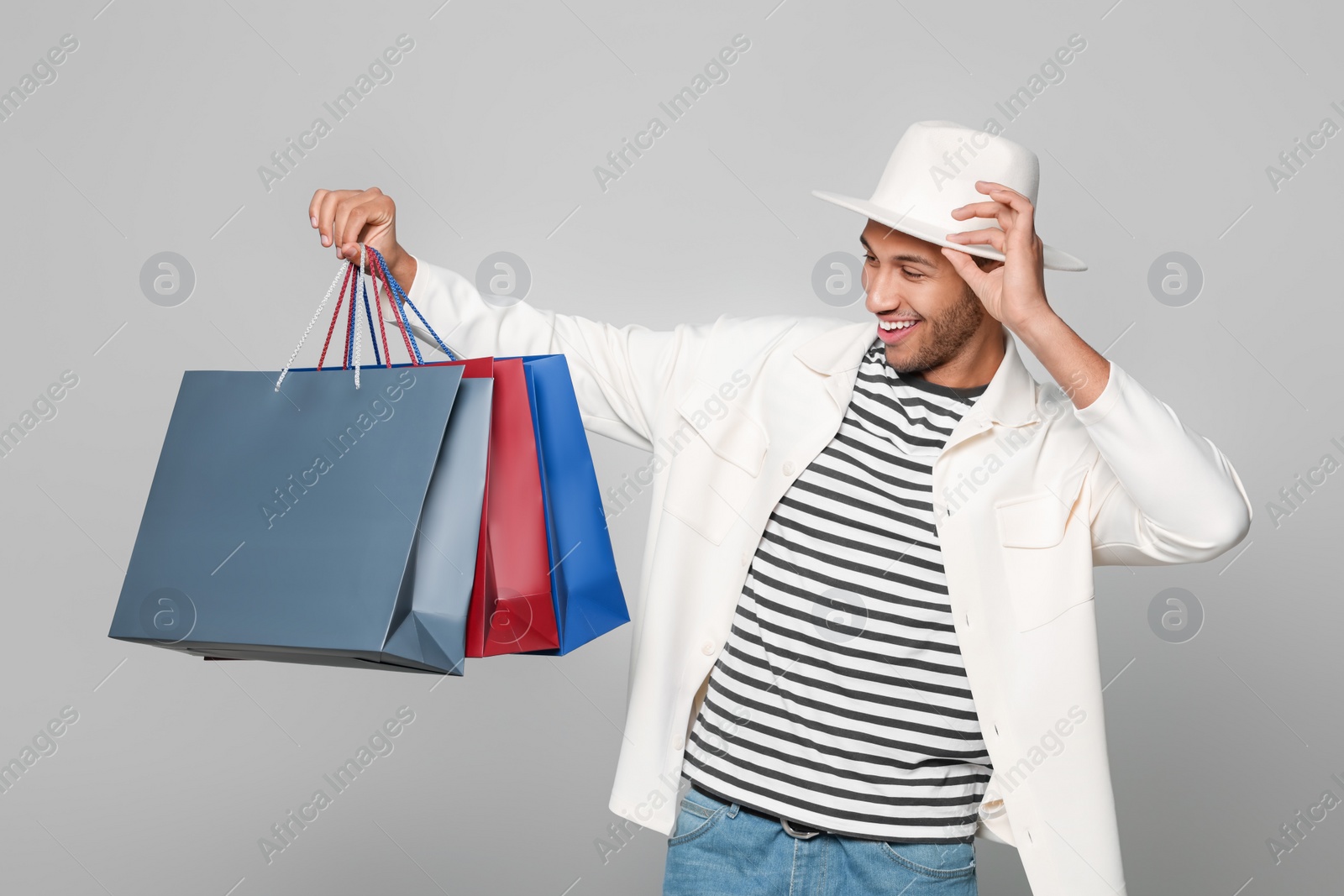 Photo of Happy African American man in hat with shopping bags on light grey background