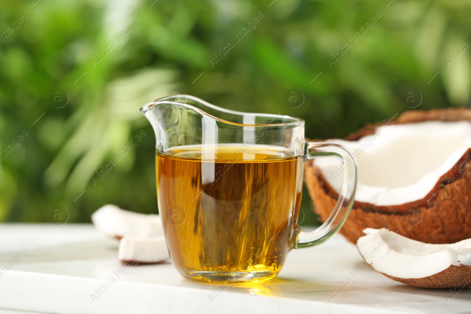 Photo of Pitcher with coconut oil on table against blurred background. Healthy cooking