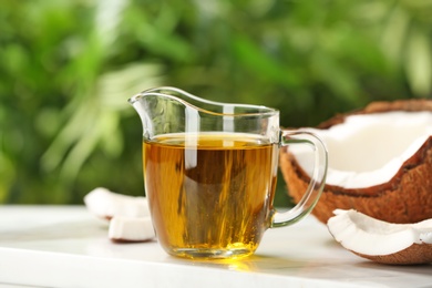 Photo of Pitcher with coconut oil on table against blurred background. Healthy cooking