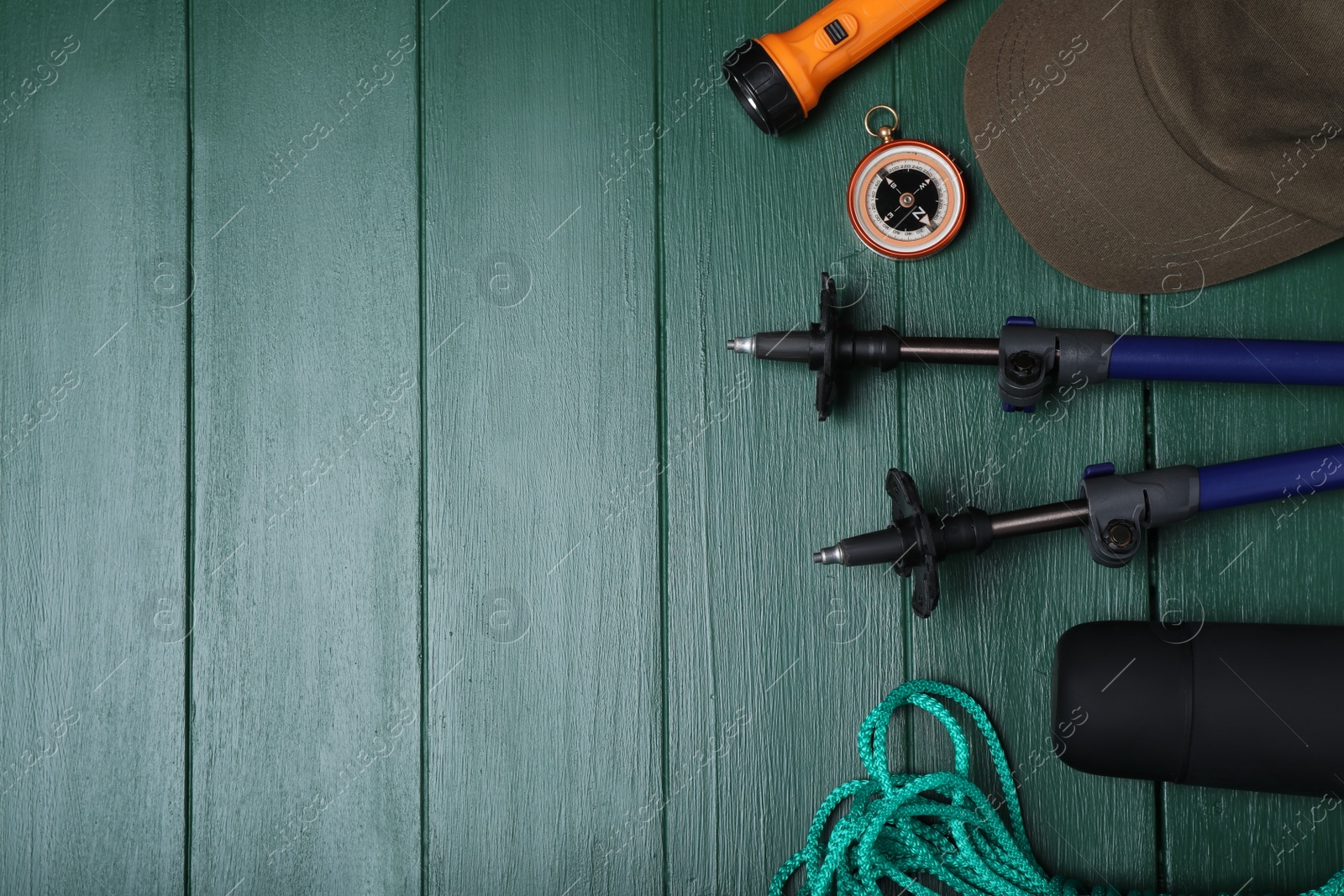 Photo of Flat lay composition with trekking poles and other hiking equipment on green wooden background, space for text