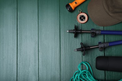 Flat lay composition with trekking poles and other hiking equipment on green wooden background, space for text