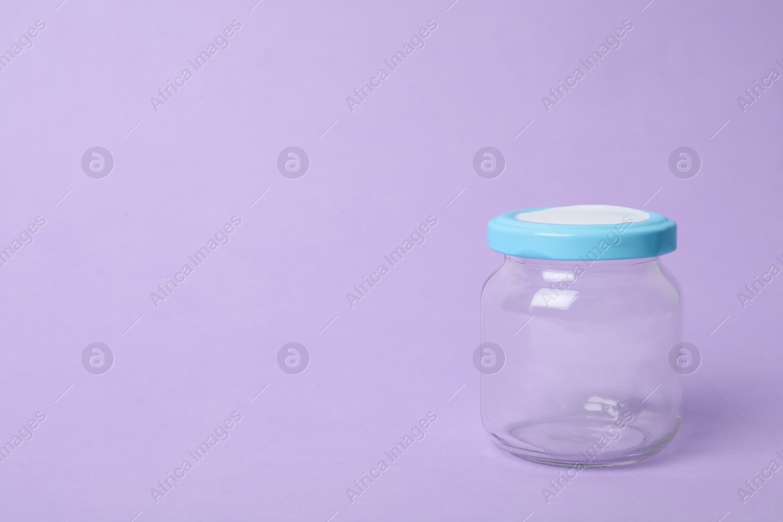 Photo of Closed empty glass jar on lilac background, space for text