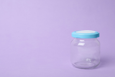 Closed empty glass jar on lilac background, space for text