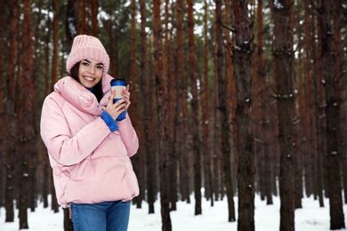 Young woman with hot drink in snowy winter forest