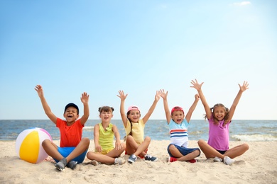 Photo of Group of happy children sitting on sand at sea beach. Summer camp