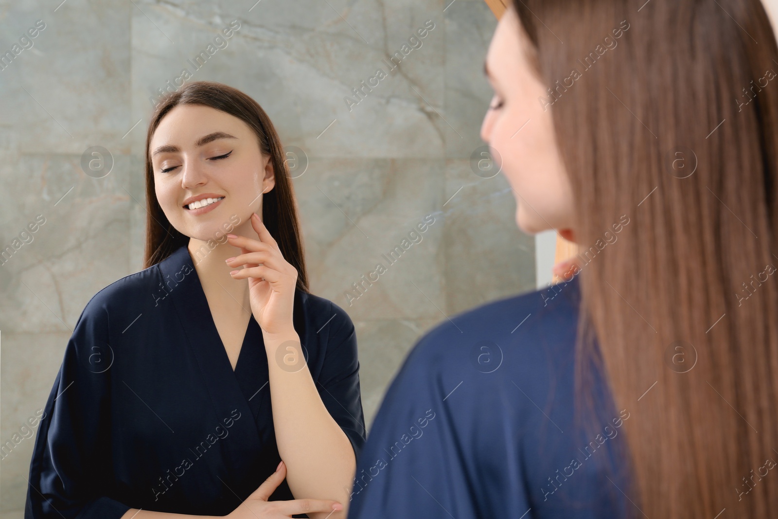 Photo of Beautiful woman in blue robe near mirror indoors