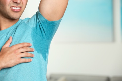 Young man with sweat stain on his clothes against blurred background, space for text. Using deodorant