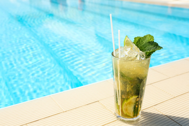 Photo of Glass of delicious mojito near swimming pool, space for text. Refreshing drink
