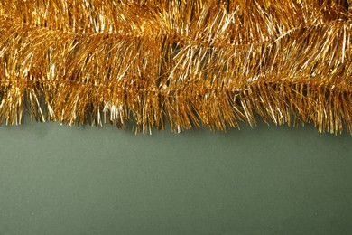 Photo of Golden tinsel on olive background, top view. Space for text