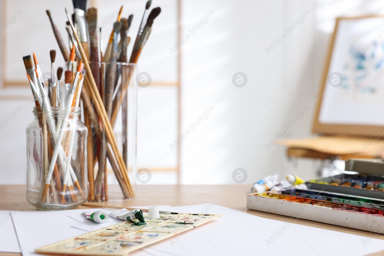 Photo of Different brushes, paints, palette and paper sheets on wooden table in studio. Space for text