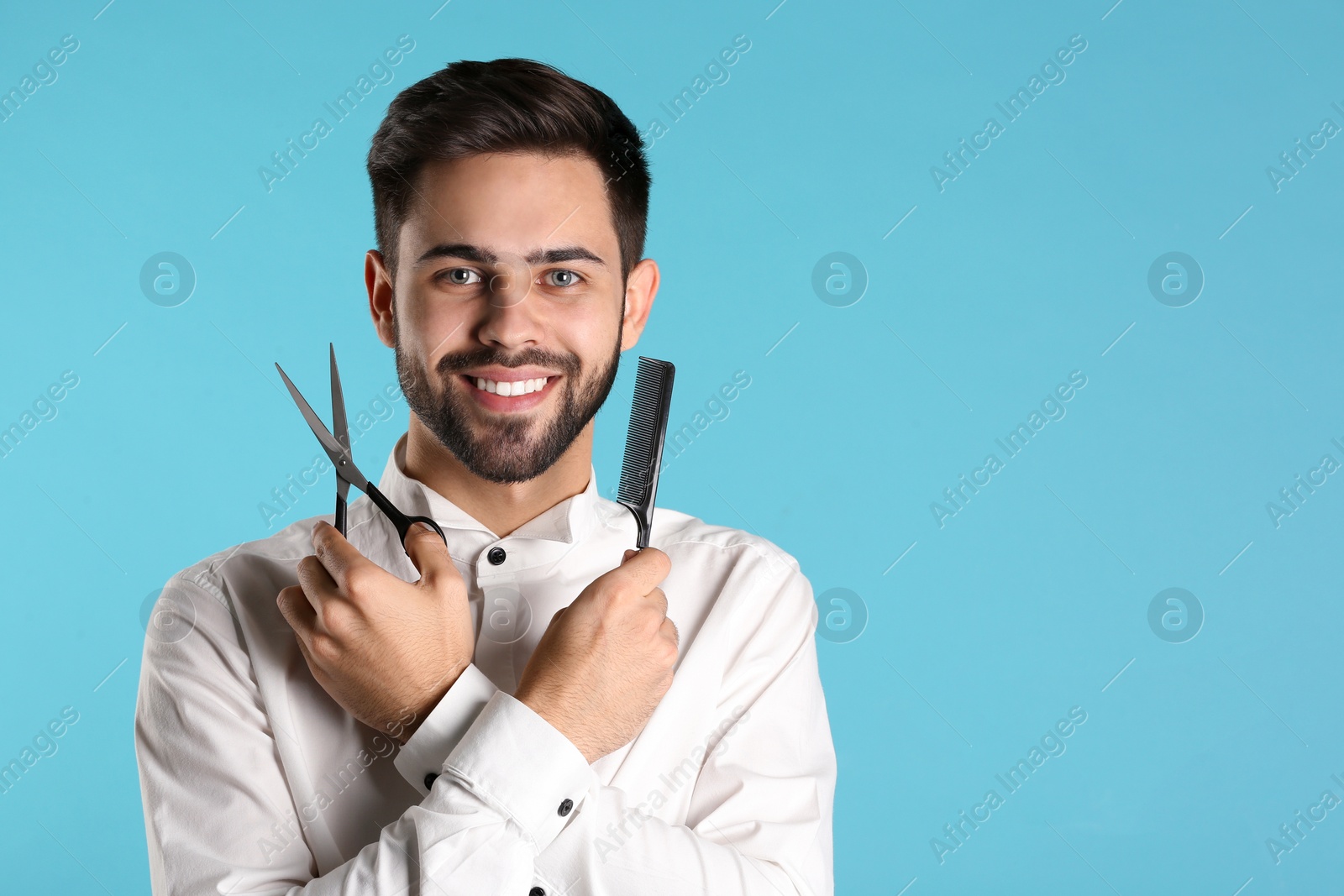 Photo of Young hairstylist holding professional scissors and comb on color background, space for text