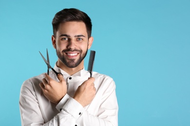 Young hairstylist holding professional scissors and comb on color background, space for text