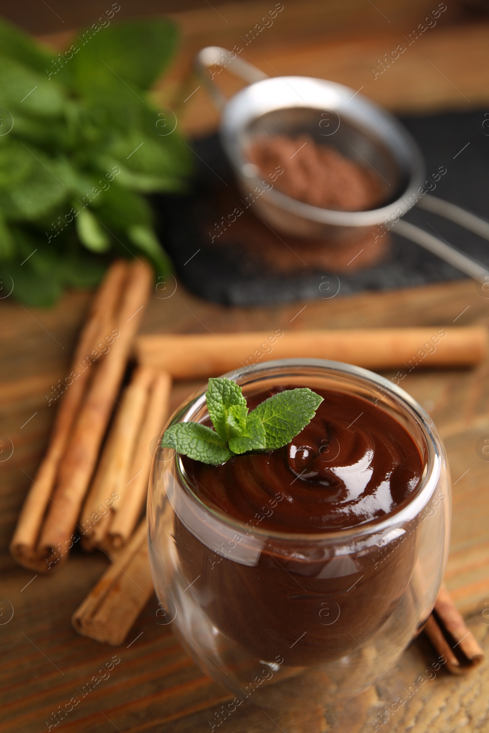 Photo of Glass of delicious hot chocolate with fresh mint and cinnamon sticks on wooden table