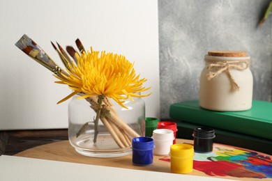 Photo of Blank white canvas, yellow chrysanthemum and different painting tools on wooden table