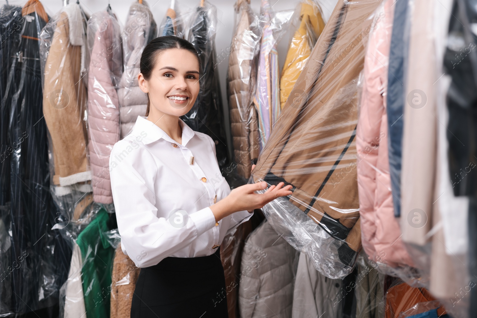 Photo of Dry-cleaning service. Happy worker choosing clothes from rack indoors