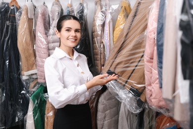 Photo of Dry-cleaning service. Happy worker choosing clothes from rack indoors