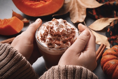 Woman holding tasty pumpkin latte at grey table, closeup