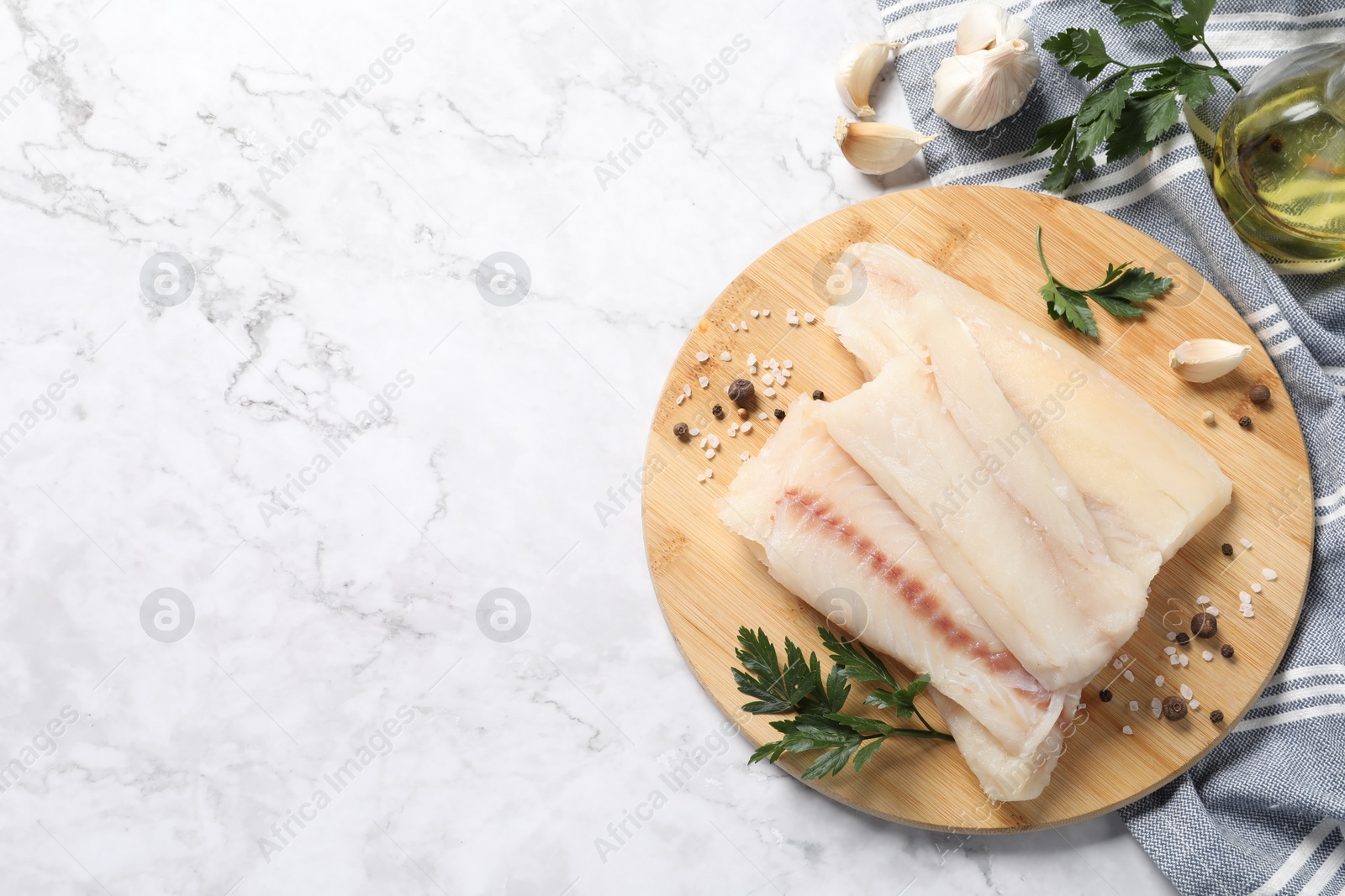 Photo of Pieces of raw cod fish, spices and parsley on white marble table, top view. Space for text